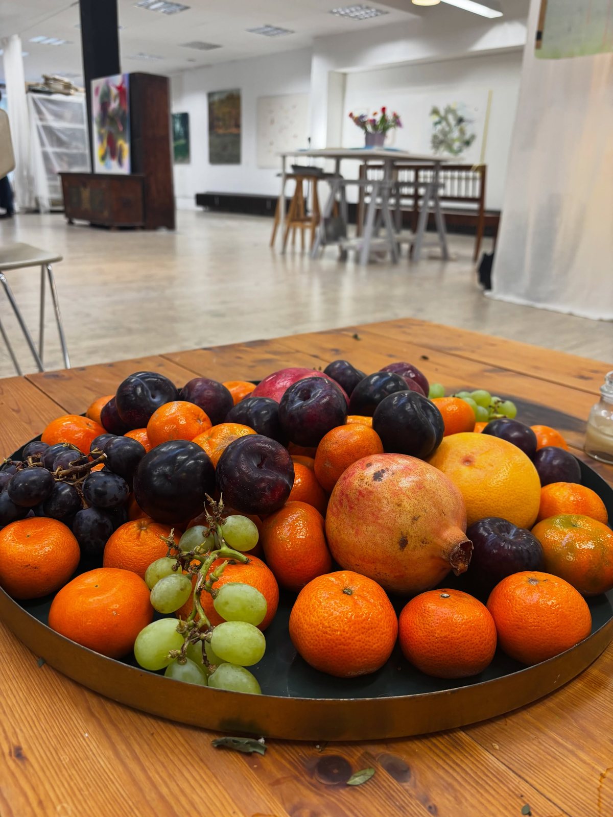 Blick in den hellen Atelierraum mit Arbeitstischen, Bildern und einer Schale Obst
